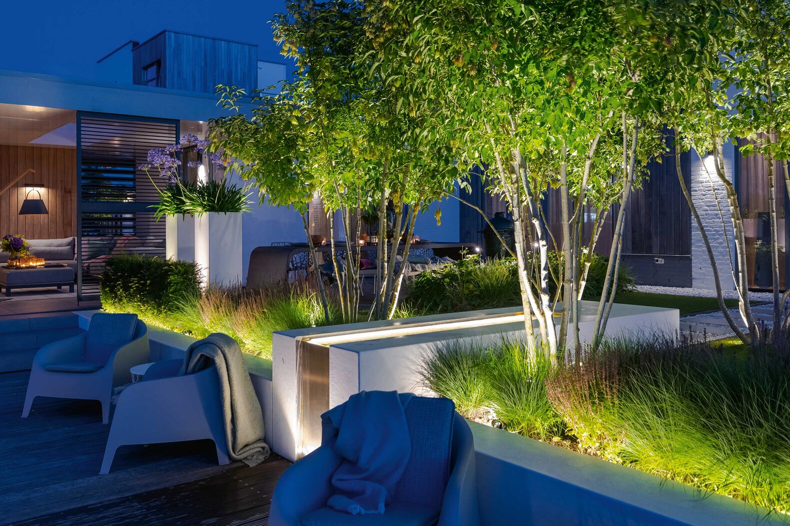 Mit Strahlern an der Wand und unterhalb von Büschen und Bäumen lässt sich der Aussenbereich effektvoll illuminieren. Green Style.